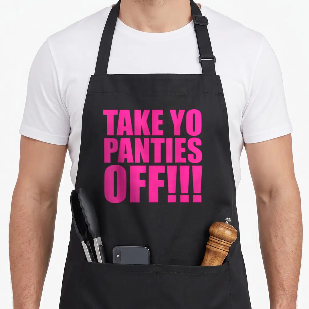 Panty class funny apron - Pink block letters reading TAKE YO PANTIES OFF!!! stacked vertically on a black background — shown on a black cotton canvas apron against a white background
