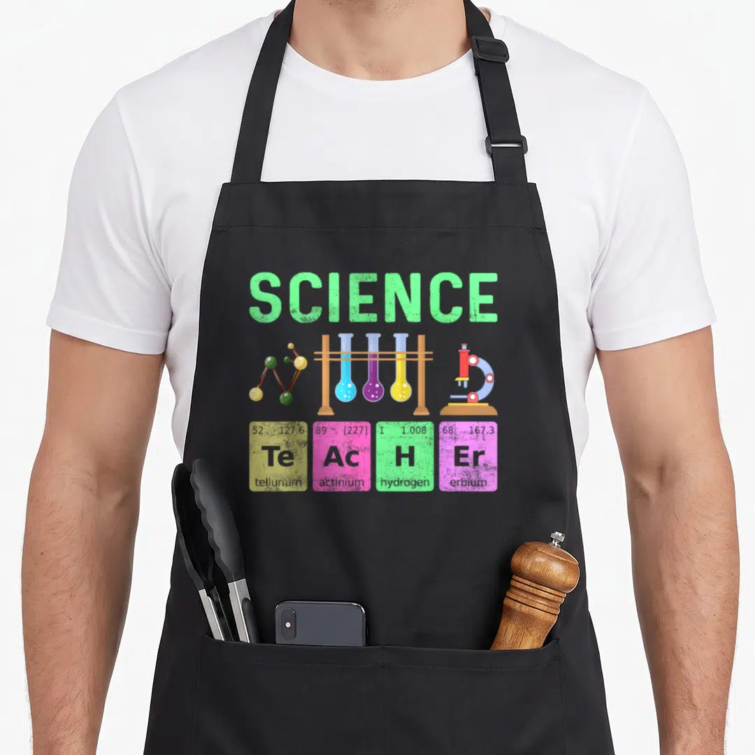 Typography teacher apron - SCIENCE text above test tubes and four element squares spelling TEACHER in green blue purple — shown on a black cotton canvas apron against a white background