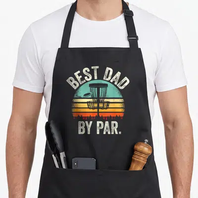 Par golf apron - Retro sun graphic with disc golf basket and text best dad by par — shown on a black cotton canvas apron against a white background