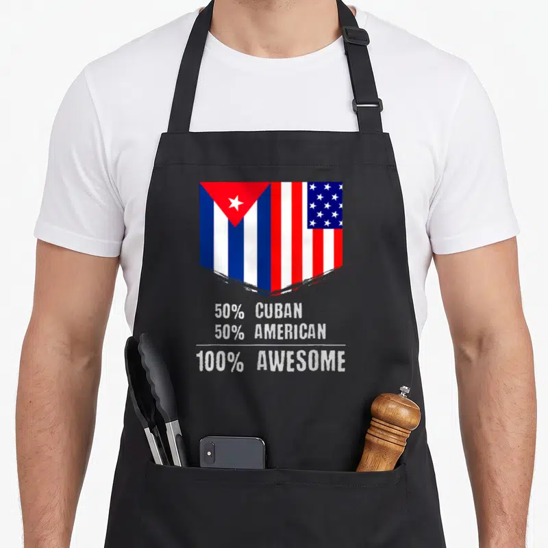 Cuban patriotic apron - Shield merging Cuban and USA flags above white 50% CUBAN 50% AMERICAN 100% AWESOME text — shown on a black cotton canvas apron against a white background