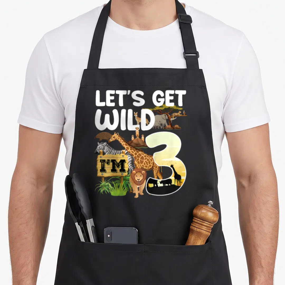 Animal 3rd birthday apron - Cartoon giraffe lion zebra and number 3 with sunset and Let's Get Wild text — shown on a black cotton canvas apron against a white background