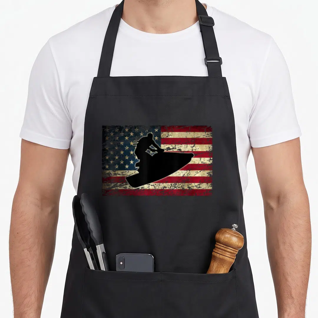 Jet american flag apron - Black jet ski silhouette over distressed red white and blue American flag pattern — shown on a black cotton canvas apron against a white background