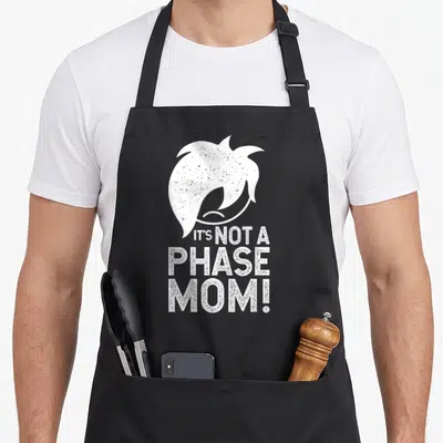 Phase goth apron - White emo hair silhouette and It's Not a Phase Mom text in distressed font — shown on a black cotton canvas apron against a white background