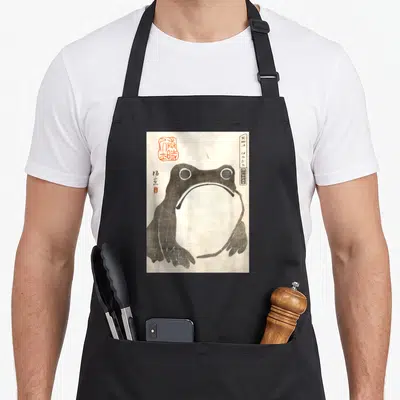 Mcma frog aprons - Watercolor frog with open mouth, Japanese text, and red seal on black fabric — shown on a black cotton canvas apron against a white background