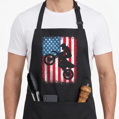 Dirt 4th of july apron - Grey motocross rider silhouette on distressed red white blue American flag background — shown on a black cotton canvas apron against a white background
