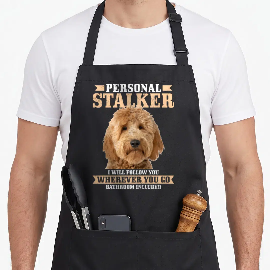Stalker personal chef apron - Distressed tan and white dog portrait with Personal Stalker text and three-line quote — shown on a black cotton canvas apron against a white background