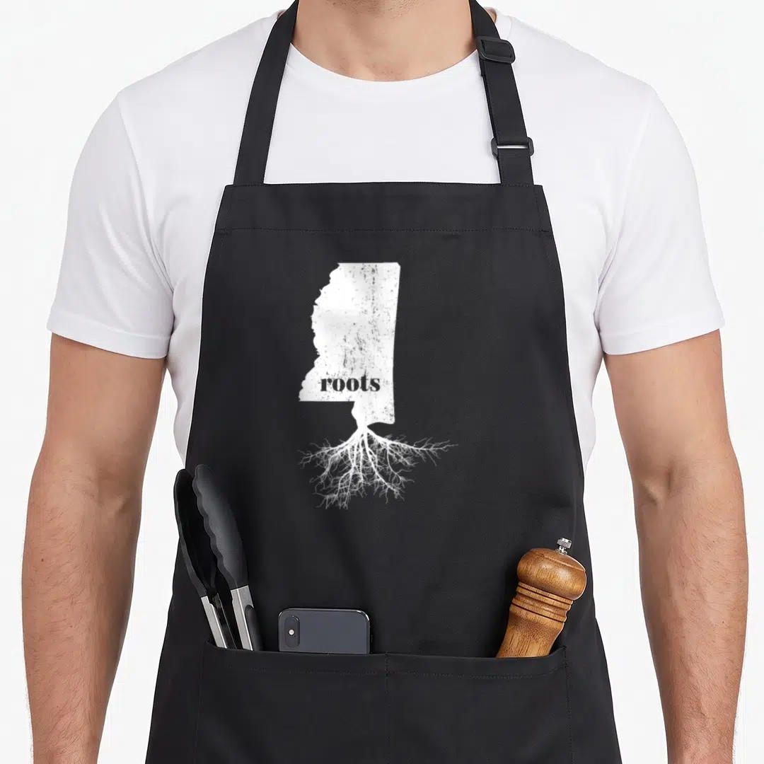 Root mississippi boy apron - White Mississippi state map silhouette with grey roots text and extending white root — shown on a black cotton canvas apron against a white background