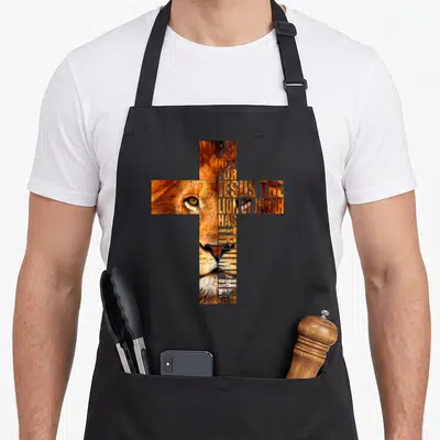 Religious lions apron - Cross shape formed by text reading FEAR NOT FOR JESUS THE LION OF JUDAH HAS TRIUMPHED filled — shown on a black cotton canvas apron against a white background