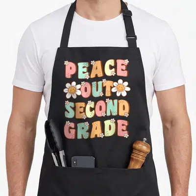 Peace second 2nd apron - Stacked colorful text reading PEACE OUT SECOND GRADE with white daisies in retro cartoon style — shown on a black cotton canvas apron against a white background
