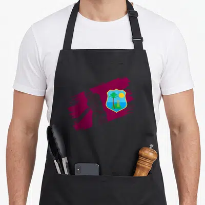 West cricket apron - White line-art cricketer over maroon stroke next to tropical shield with palm tree and stumps — shown on a black cotton canvas apron against a white background