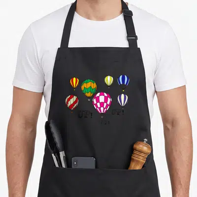 Youth balloon apron - Seven striped hot air balloons in red, yellow, green, blue, pink, and purple with three UP! — shown on a black cotton canvas apron against a white background