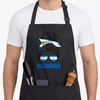 Flag nicaraguan girl apron - Cartoon messy bun with blue white gold flag headband and sunglasses reflecting flag above — shown on a black cotton canvas apron against a white background