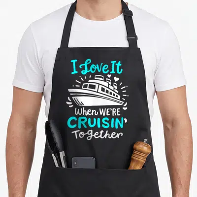 Cruise novelty apron - White cruise ship with cyan text and hearts on black background — shown on a black cotton canvas apron against a white background