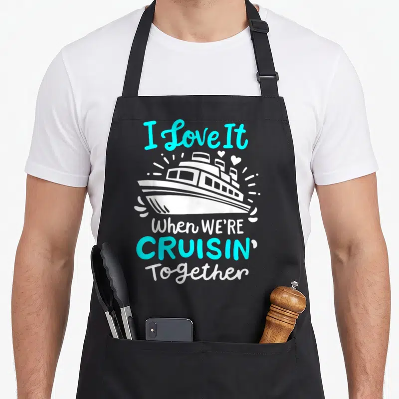 Cruise novelty apron - White cruise ship with cyan text and hearts on black background — shown on a black cotton canvas apron against a white background