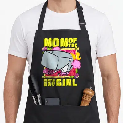 Pearl mother's apron - Cartoon grey shark with pink hair and yellow Mom of the Birthday Girl text — shown on a black cotton canvas apron against a white background