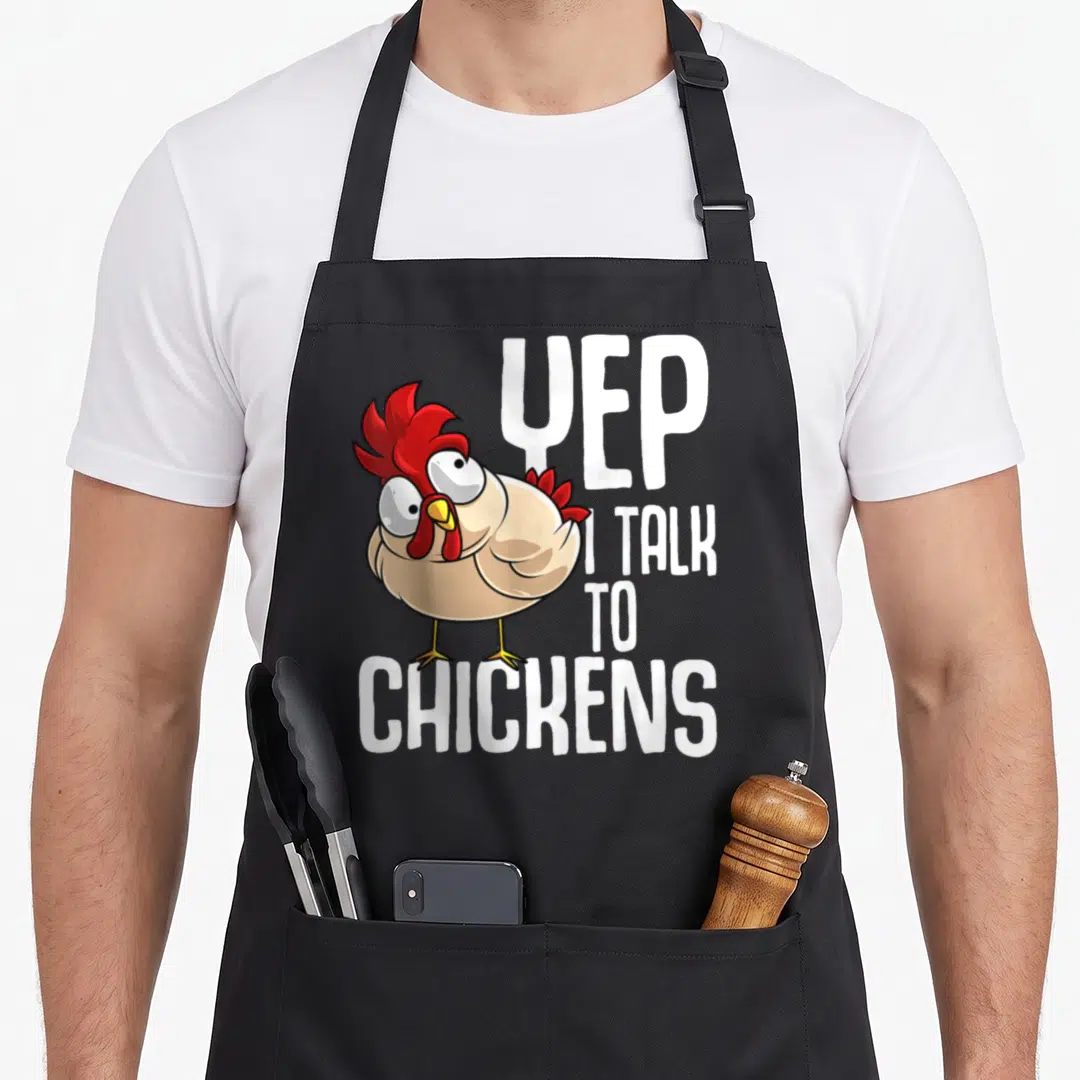 Talk chicken apron - Cartoon chicken illustration with YEP I TALK TO CHICKENS text in white beige and red — shown on a black cotton canvas apron against a white background