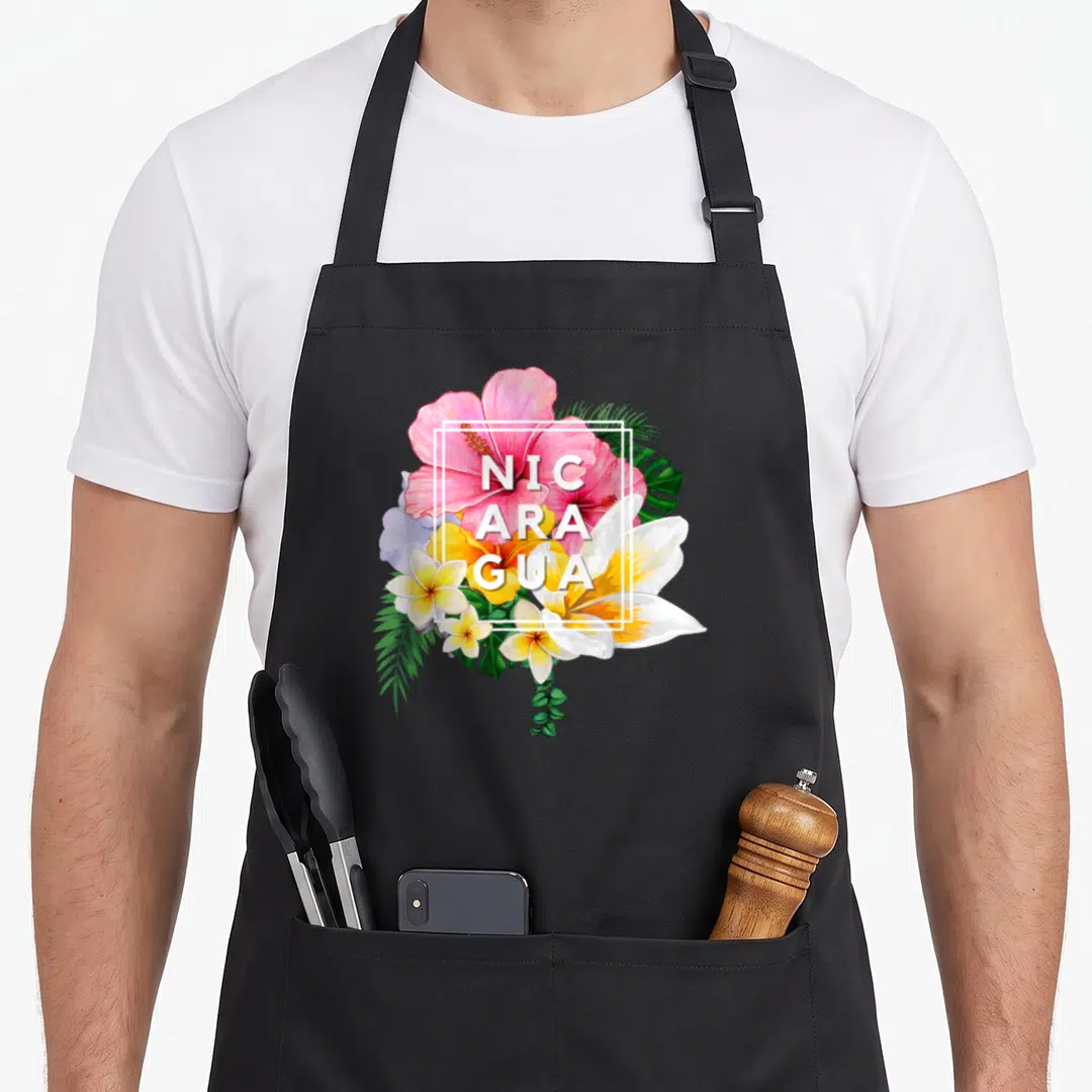 Nicaragua floral apron - Pink yellow white and green tropical flowers with NIC ARA GUA text in white square frame — shown on a black cotton canvas apron against a white background