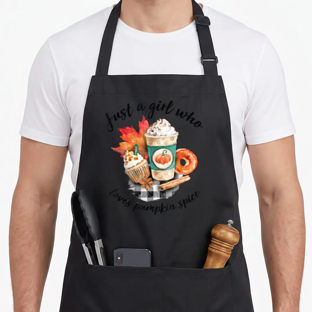 Enthusiast spice apron - Watercolor pumpkin latte, cupcake, donut, and leaf on plaid with arched text — shown on a black cotton canvas apron against a white background
