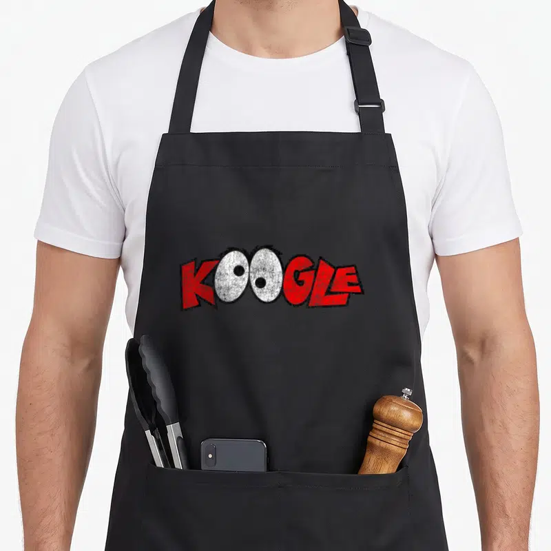 Koogle butter apron - KOOGLE text with two cartoon eyes replacing the O letters in red and white — shown on a black cotton canvas apron against a white background