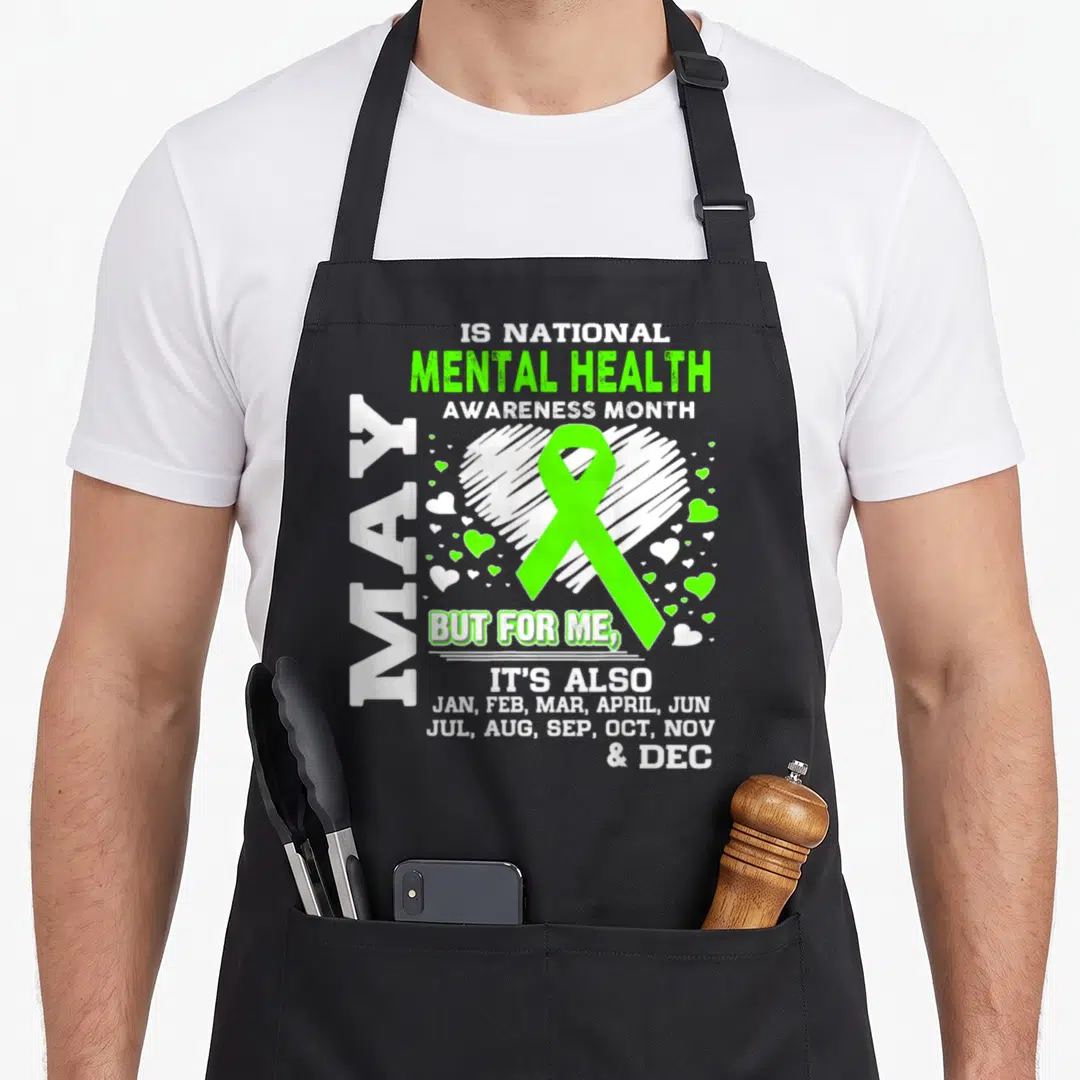 May mental health awareness apron - Lime green ribbon over white sketched heart with vertical MAY and full list — shown on a black cotton canvas apron against a white background