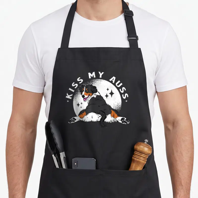 Kiss australian aprons - Line art dog with KISS MY AUSS text over white circle and stars — shown on a black cotton canvas apron against a white background