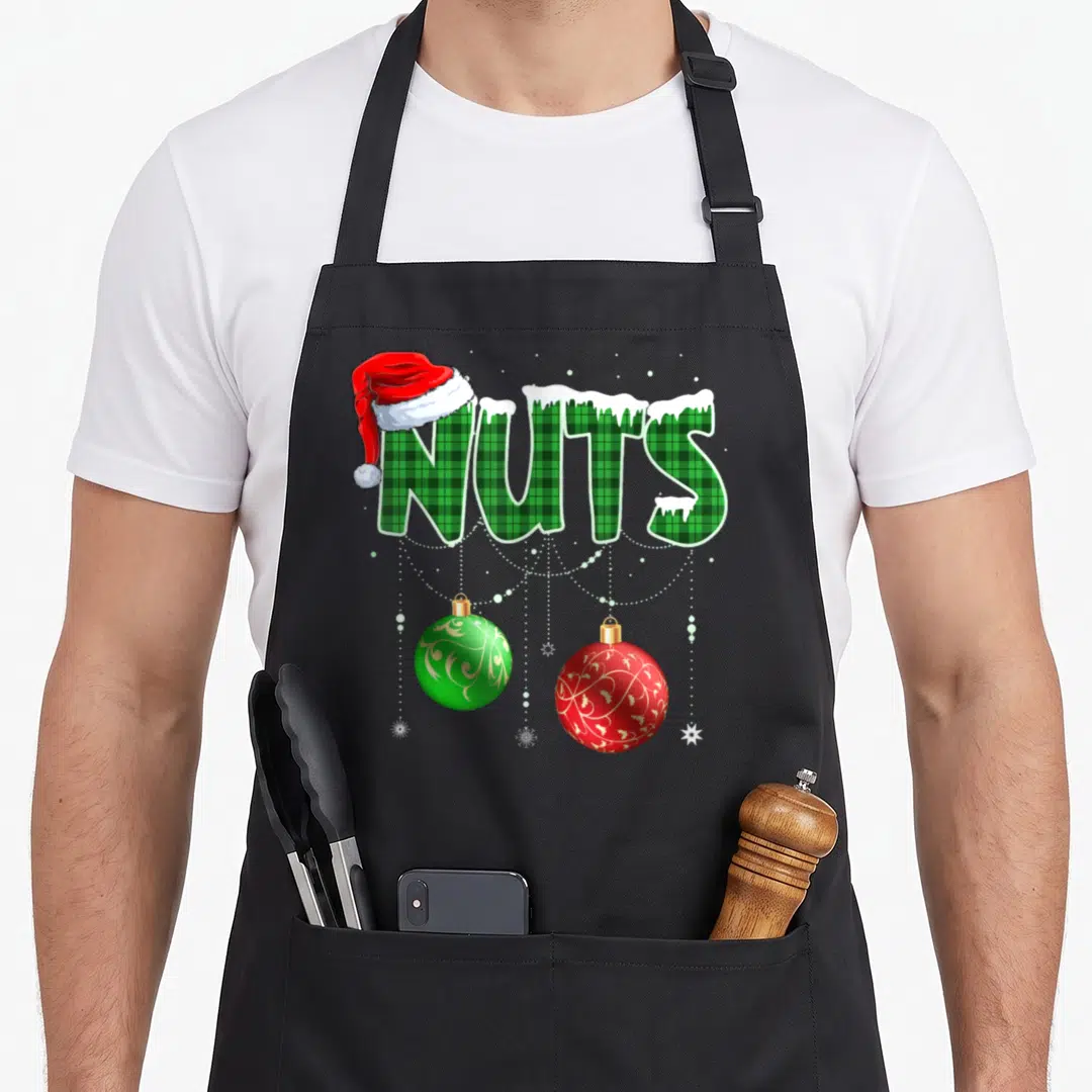 Chestnut family christmas aprons - NUTS text in green plaid with Santa hat, snow, and two hanging red and green — shown on a black cotton canvas apron against a white background