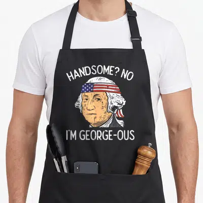 Handsome 4th of july apron - George Washington portrait with flag headband and Handsome George-ous pun text — shown on a black cotton canvas apron against a white background