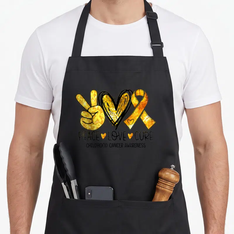 Peace cure ribbon apron - Gold peace sign heart and ribbon with PEACE LOVE CURE text — shown on a black cotton canvas apron against a white background