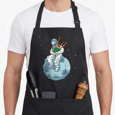 Scottish bagpipes apron - Cartoon astronaut in white suit playing green bagpipes while sitting on a light blue moon — shown on a black cotton canvas apron against a white background