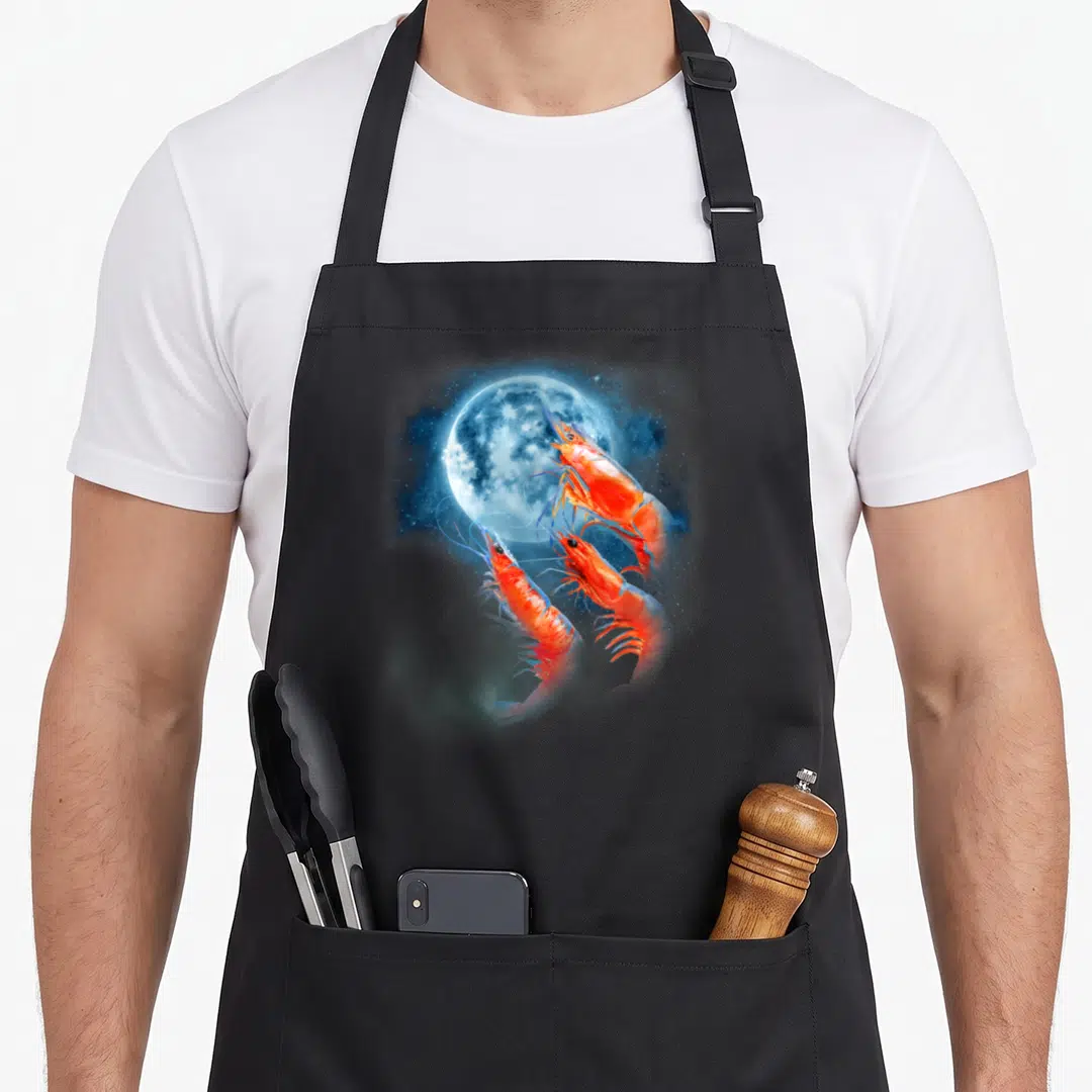 Prawn howling moon apron - Three realistic shrimp swimming up towards a blue moon in a starry nebula — shown on a black cotton canvas apron against a white background