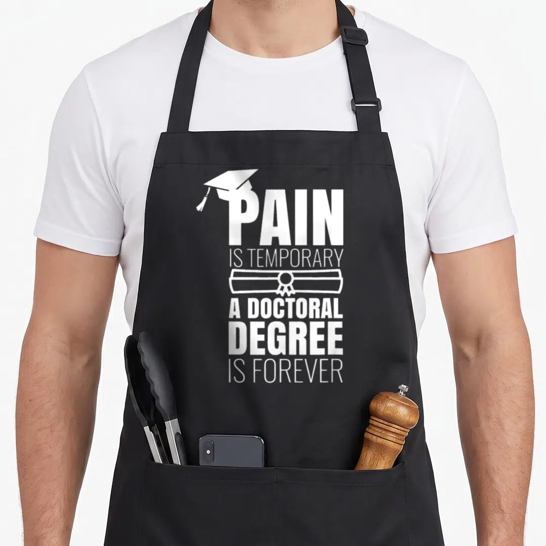Phd ph scale apron - White stacked text PAIN IS TEMPORARY A DOCTORAL DEGREE IS FOREVER with cap and diploma icons — shown on a black cotton canvas apron against a white background
