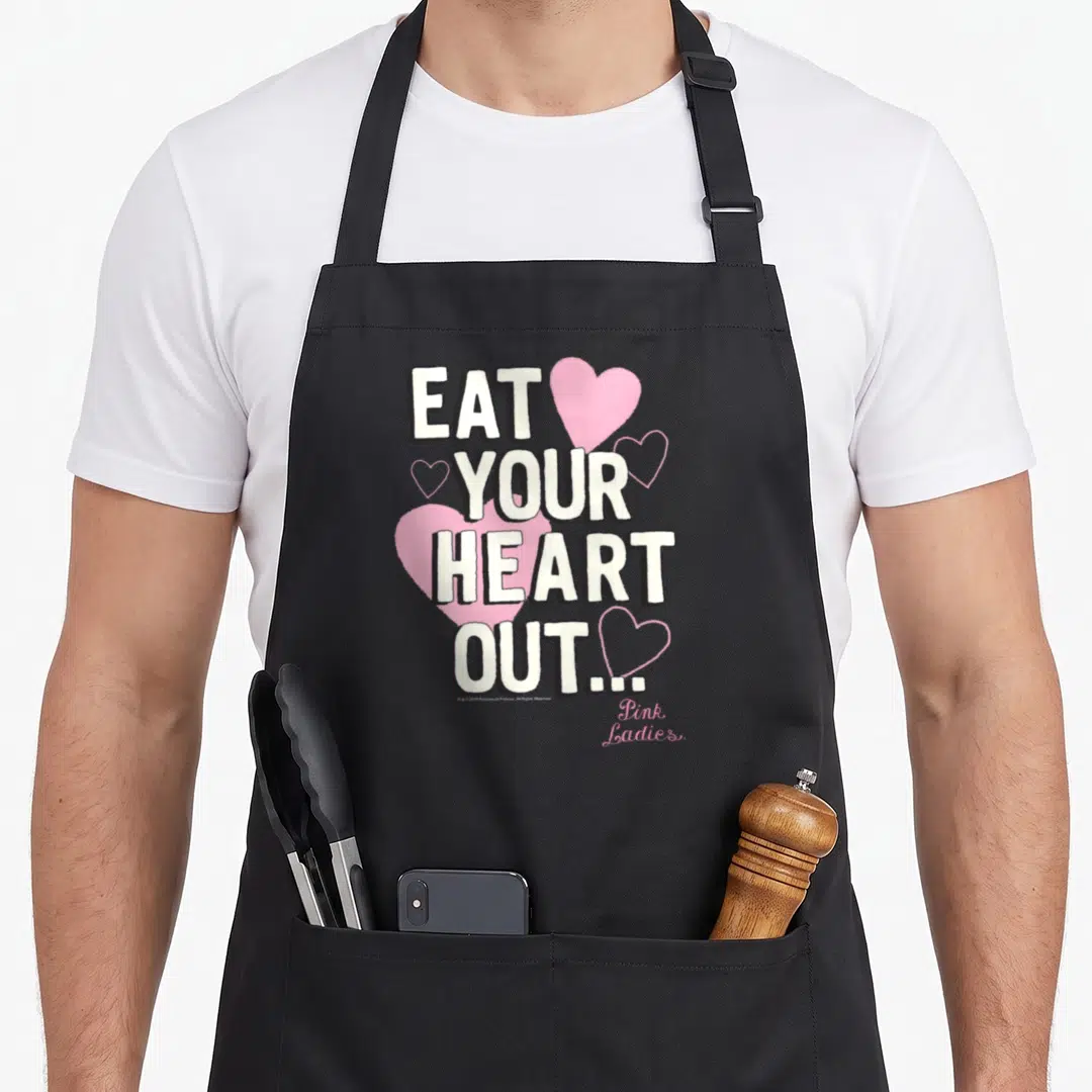 Eat grease apron - EAT YOUR HEART OUT text with pink hearts and Pink Ladies script — shown on a black cotton canvas apron against a white background