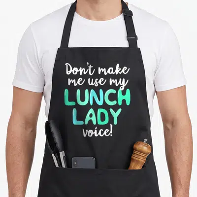 Volunteer lunch lady apron - Stacked white and teal text reading Don't make me use my LUNCH LADY voice! — shown on a black cotton canvas apron against a white background
