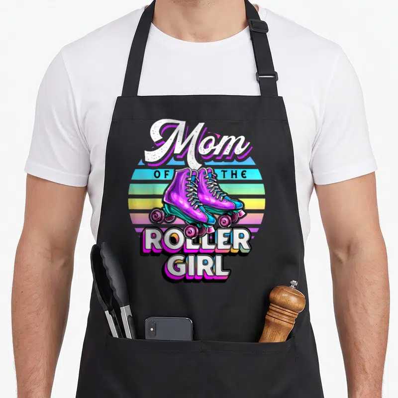 Roller skating family aprons - Mom of the Roller Girl text with purple skates on striped sunset background — shown on a black cotton canvas apron against a white background