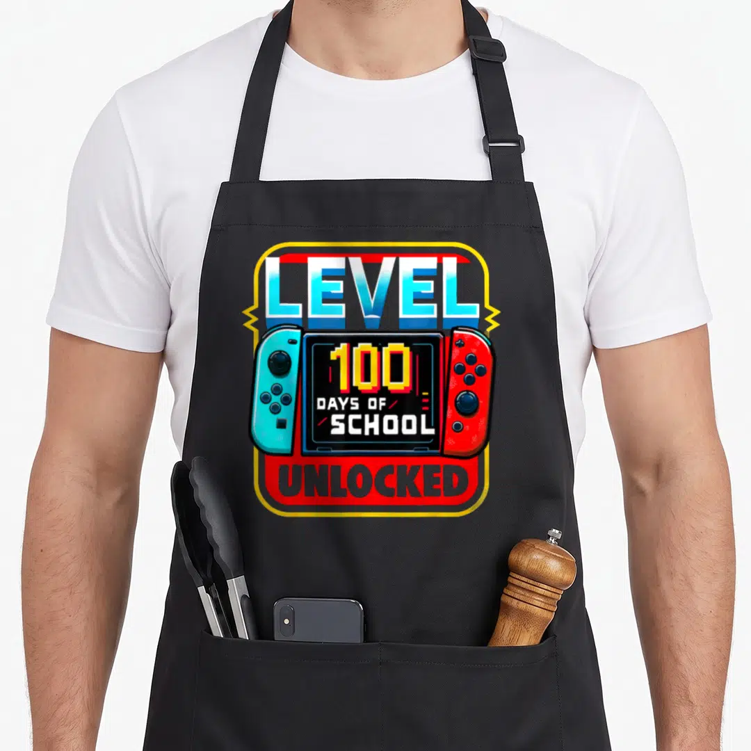 Controller game aprons - Handheld console with blue and red controllers displaying 100 days of school unlocked text — shown on a black cotton canvas apron against a white background