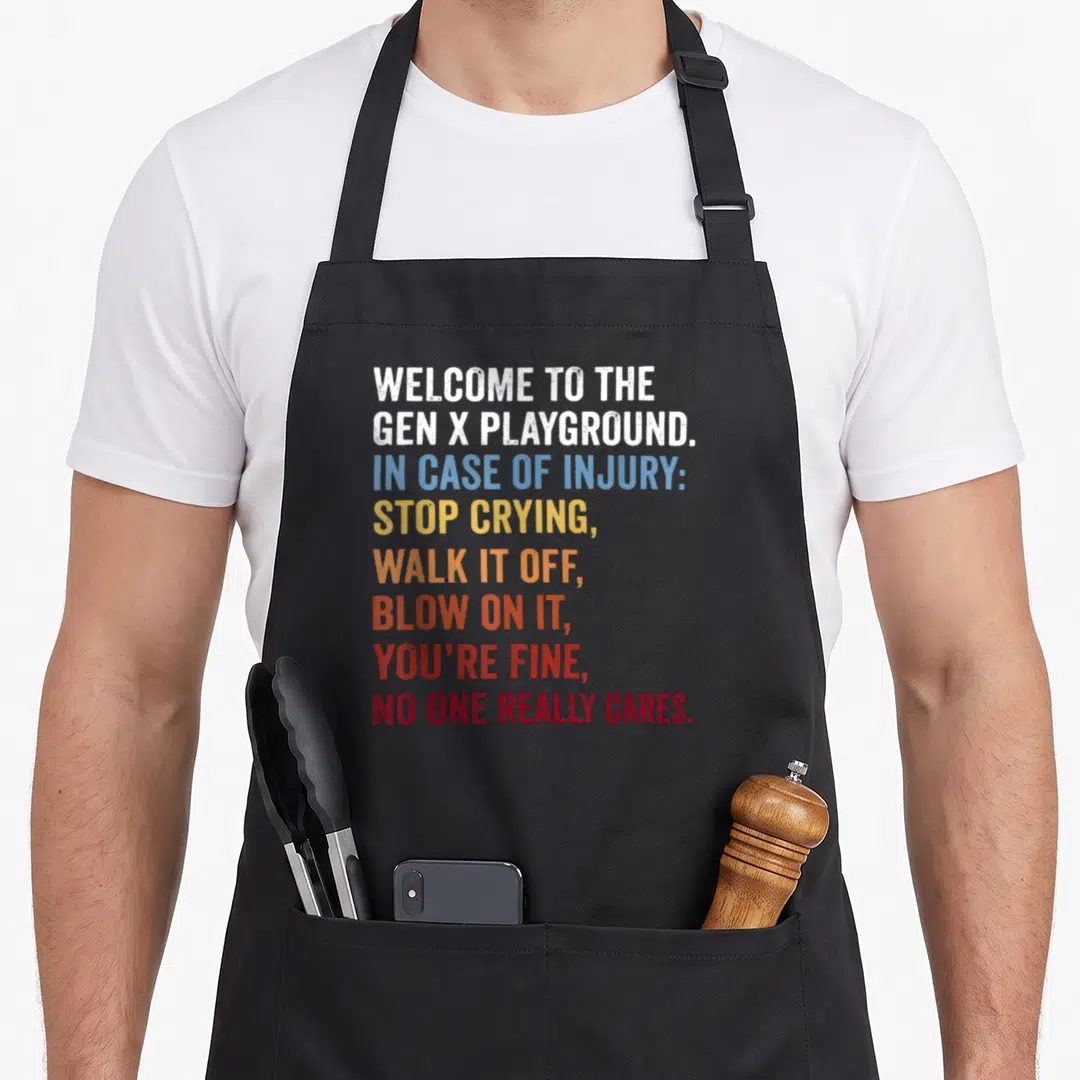 Welcome 1980s apron - Stacked colorful text reading Welcome to the Gen X Playground and injury advice — shown on a black cotton canvas apron against a white background