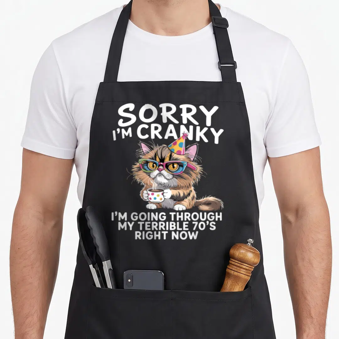 Sorry i love my cat apron - Cranky brown cat in blue and pink glasses holding coffee with white text above and below — shown on a black cotton canvas apron against a white background