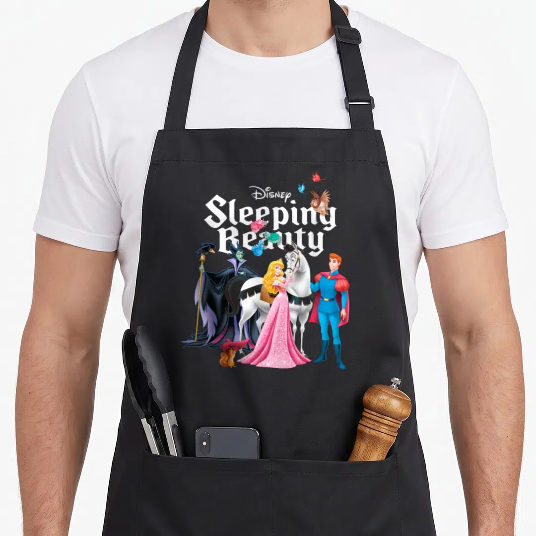 Character beauty apron - Sleeping Beauty title with Aurora, Prince Phillip, and villain in white pink blue purple black — shown on a black cotton canvas apron against a white background