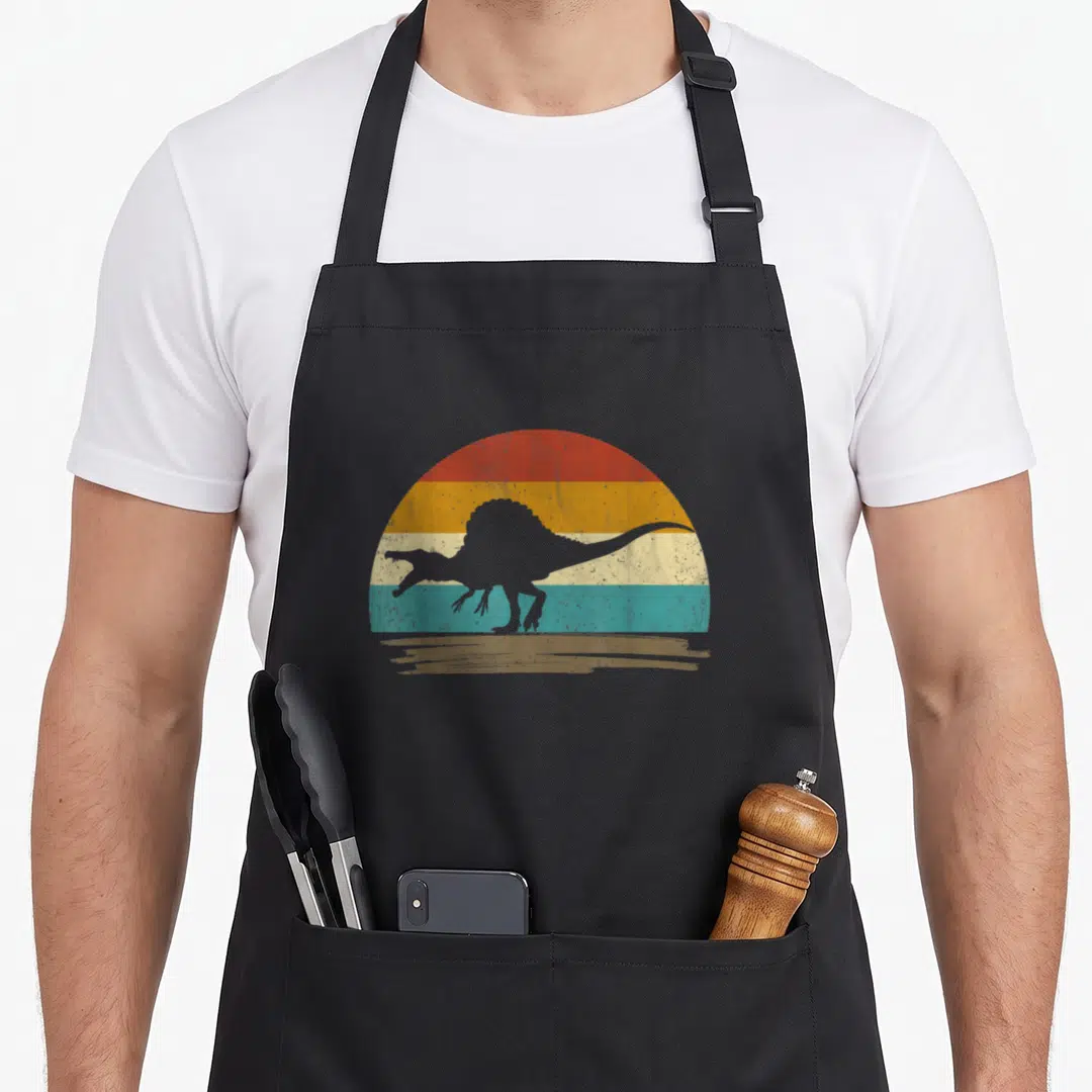 Funny spinosaurus dinosaur apron - Grey dinosaur silhouette over red orange yellow teal striped semi-circle with brown — shown on a black cotton canvas apron against a white background