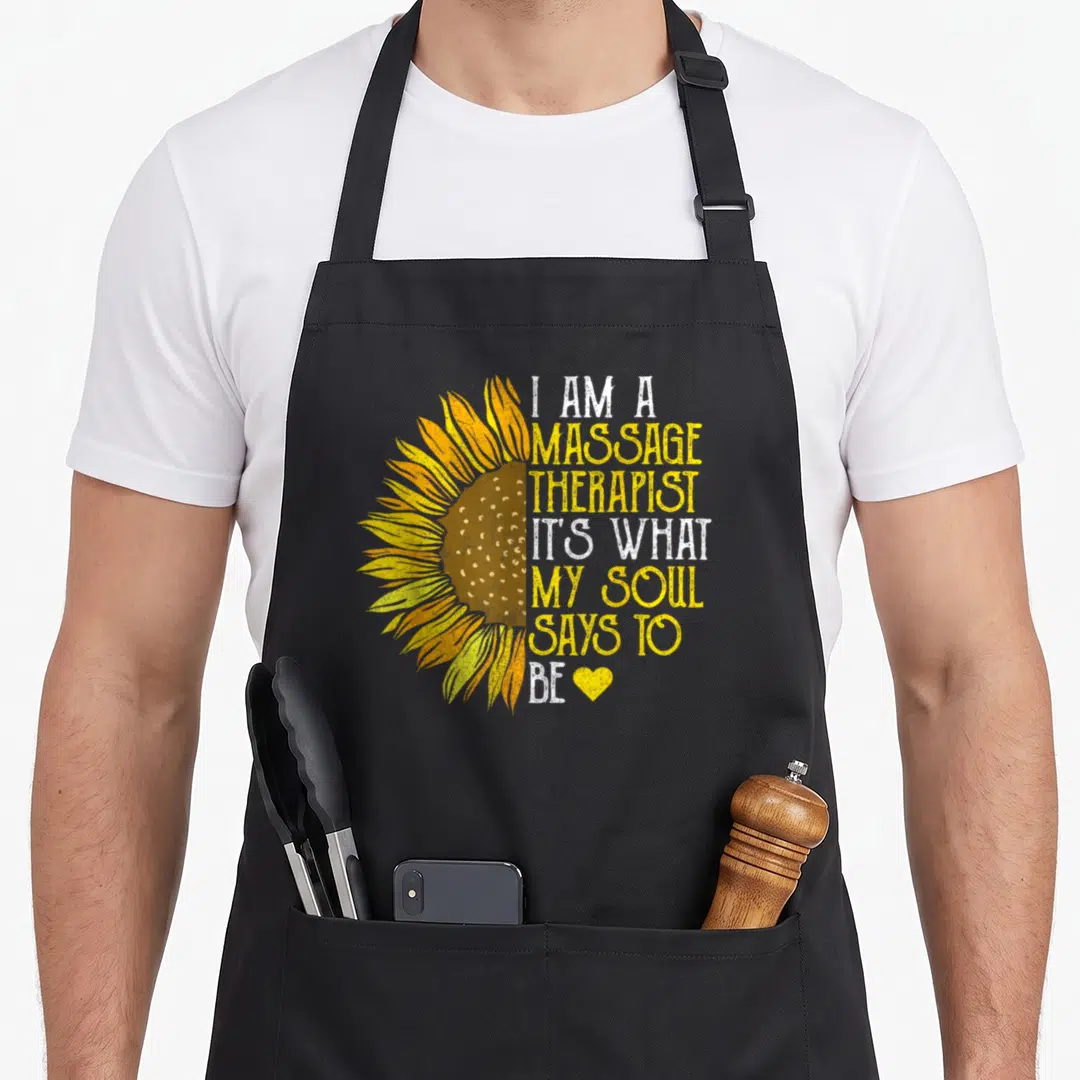 Uniform massage therapist apron - Half sunflower in yellow and brown next to stacked text reading I am a massage — shown on a black cotton canvas apron against a white background