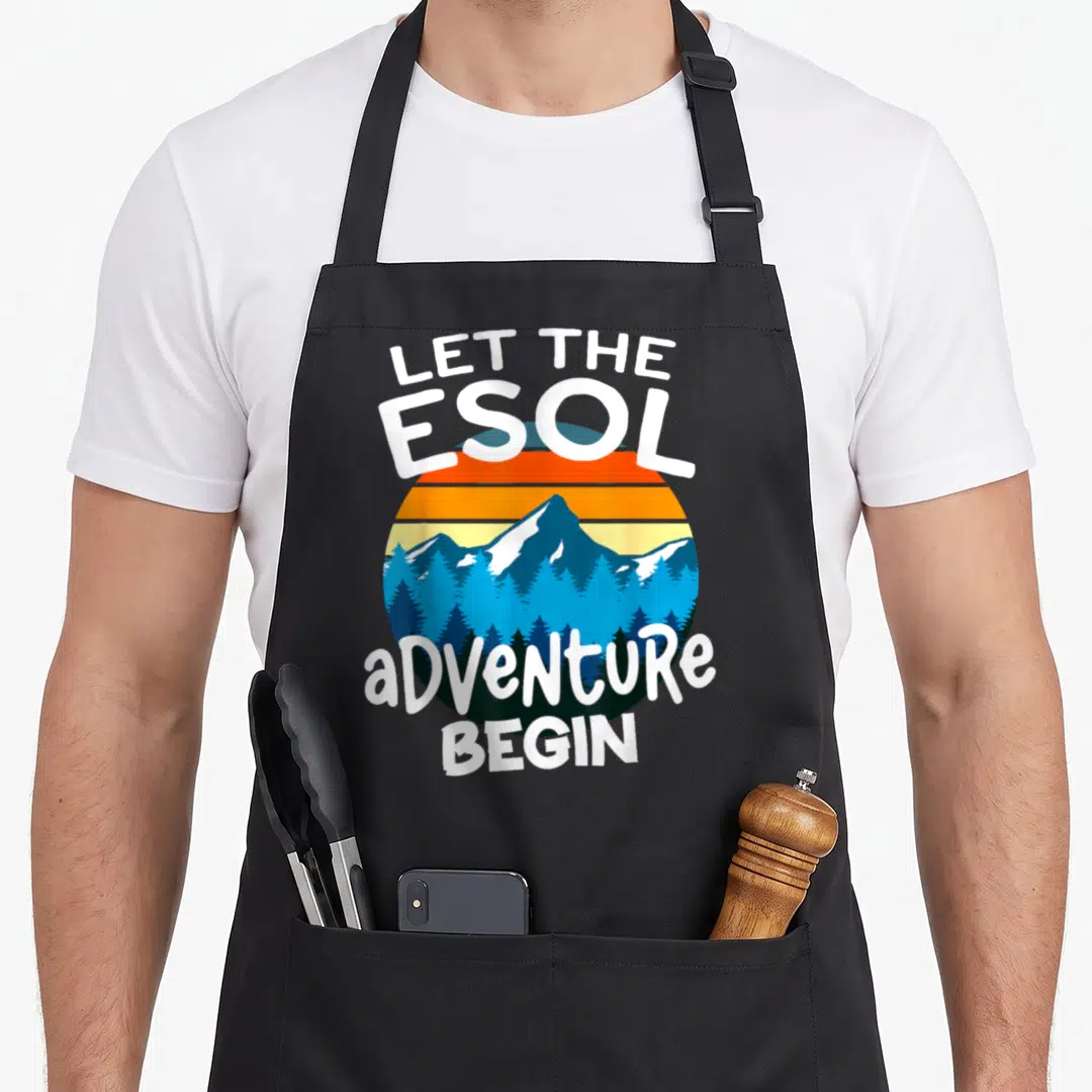 Esol teacher apron - Retro sunset circle with mountain and forest, white text reading LET THE ESOL ADVENTURE BEGIN — shown on a black cotton canvas apron against a white background