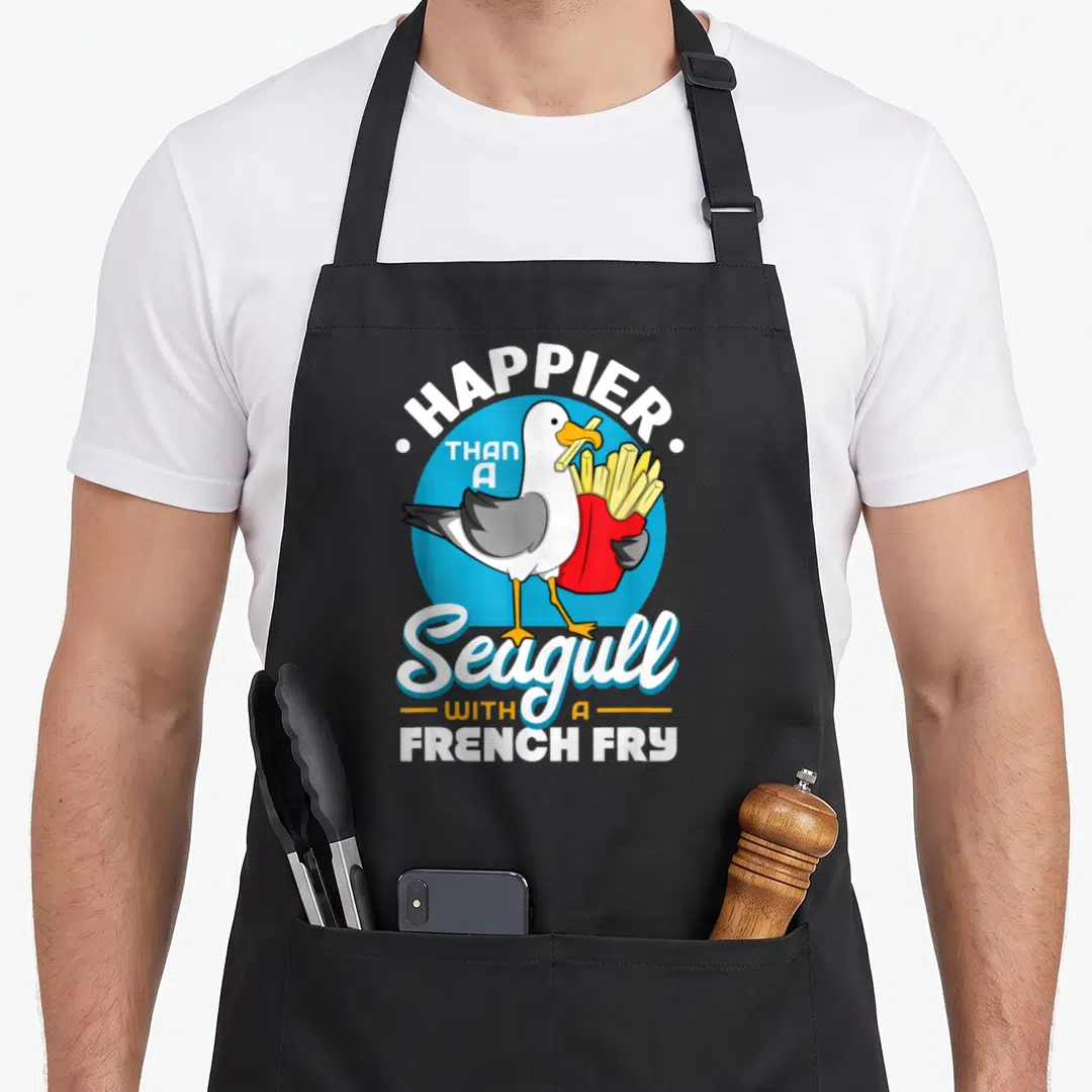 Seagull fry french apron - Cartoon seagull holding red french fries with arched text HAPPIER THAN A Seagull — shown on a black cotton canvas apron against a white background