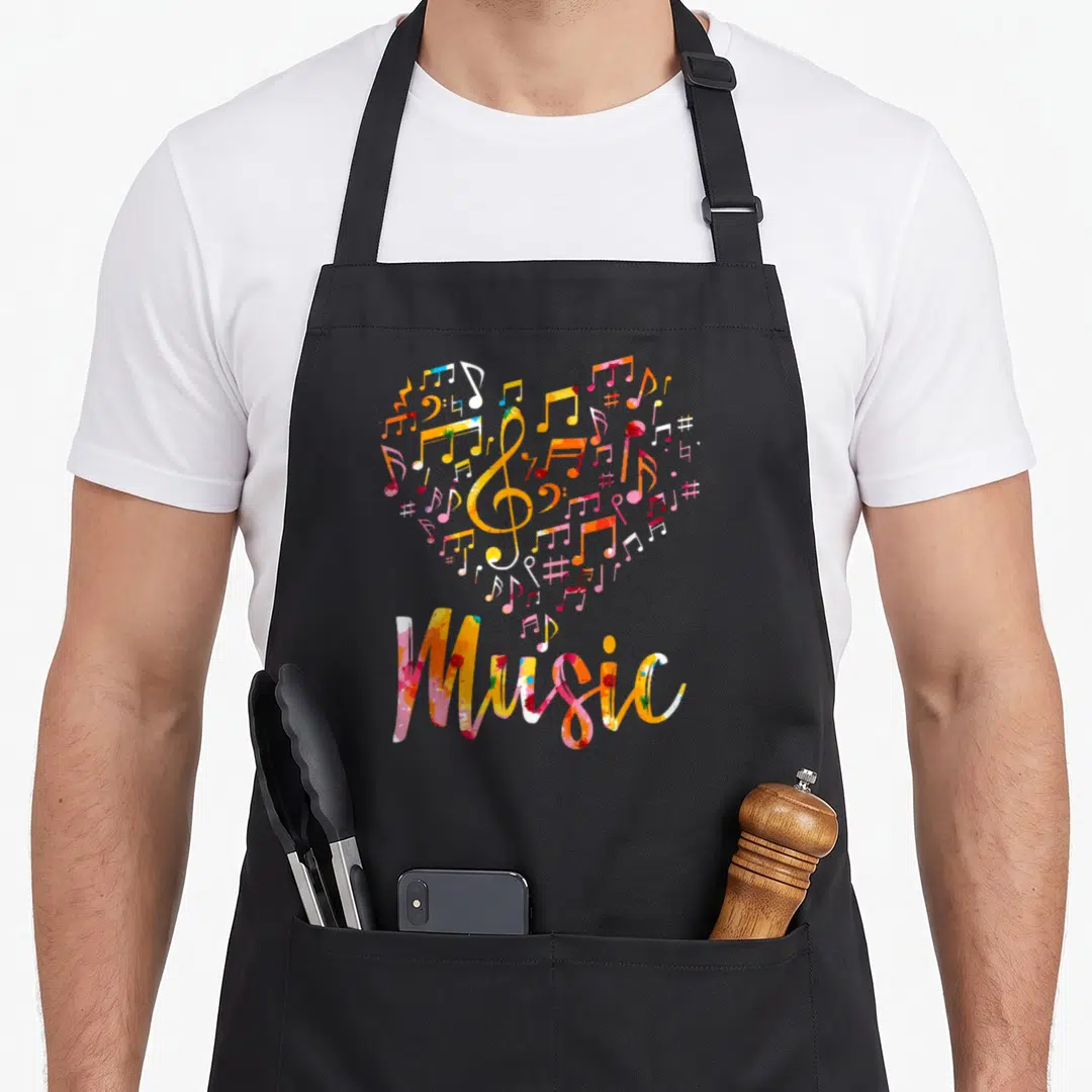 Musician music apron - Watercolor heart of musical notes and treble clef with Music text in rainbow colors — shown on a black cotton canvas apron against a white background