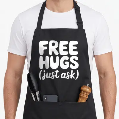 Hug unity day apron - White stacked text reading free hugs just ask on dark background — shown on a black cotton canvas apron against a white background
