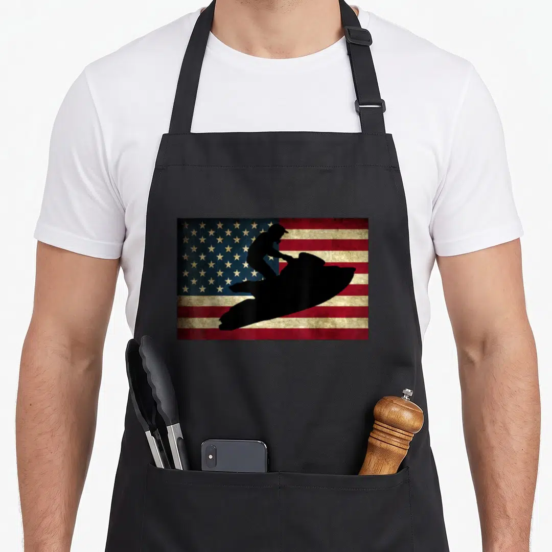 Ski jet apron - Black jet skier silhouette on distressed red white and blue American flag — shown on a black cotton canvas apron against a white background