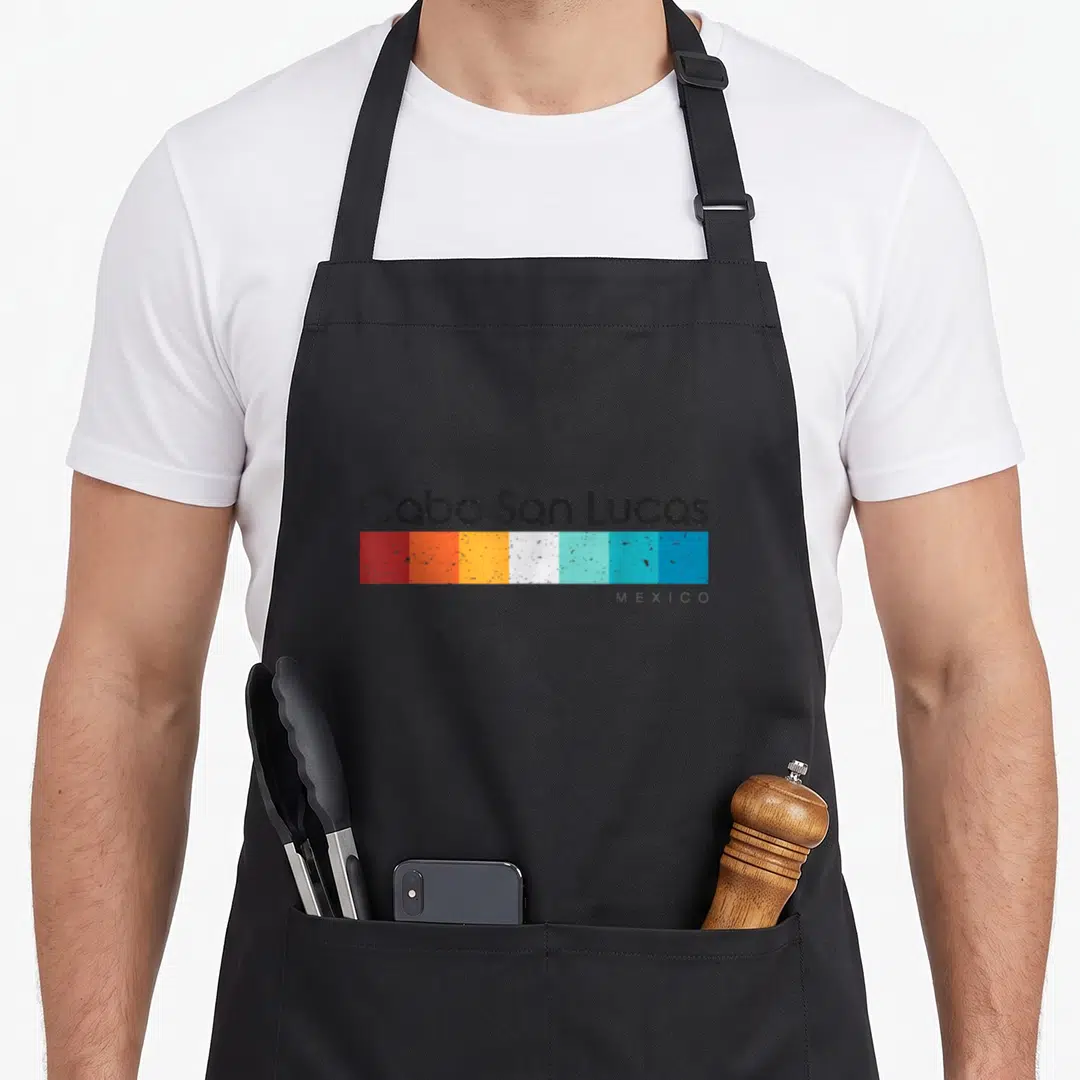 Funny cabo mexico apron - Cabo San Lucas text above seven red orange yellow white and blue rectangles with Mexico label — shown on a black cotton canvas apron against a white background
