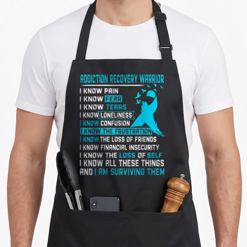 Warrior addiction recovery apron - Distressed light blue ribbon with birds and stacked white and blue text listing — shown on a black cotton canvas apron against a white background