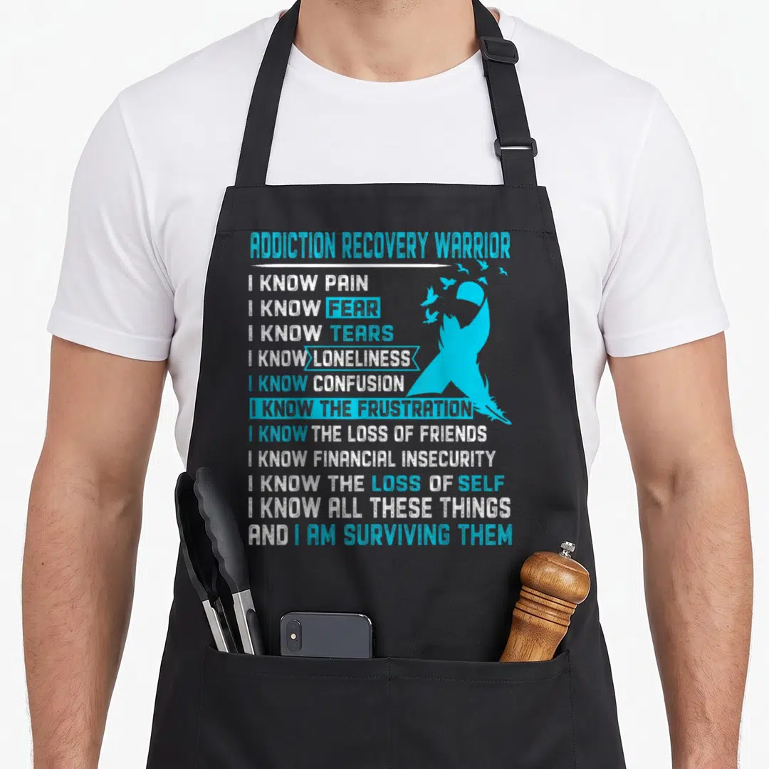 Warrior addiction recovery apron - Distressed light blue ribbon with birds and stacked white and blue text listing — shown on a black cotton canvas apron against a white background