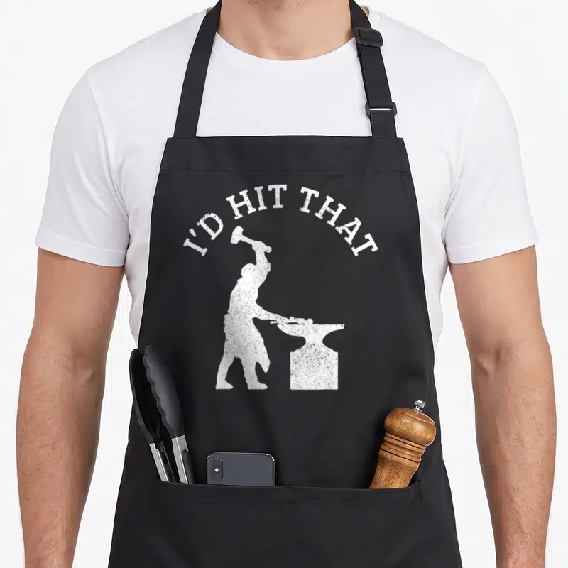 Schmied blacksmith apron - Arched I'D HIT THAT text above white blacksmith silhouette holding hammer over anvil — shown on a black cotton canvas apron against a white background