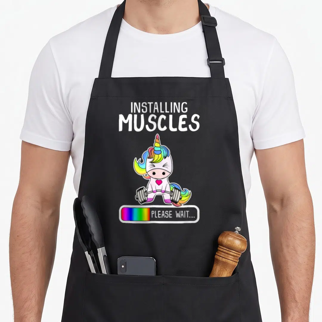 Weightlifting muscle apron - Cartoon unicorn lifting barbell with installing muscles text and rainbow loading bar — shown on a black cotton canvas apron against a white background